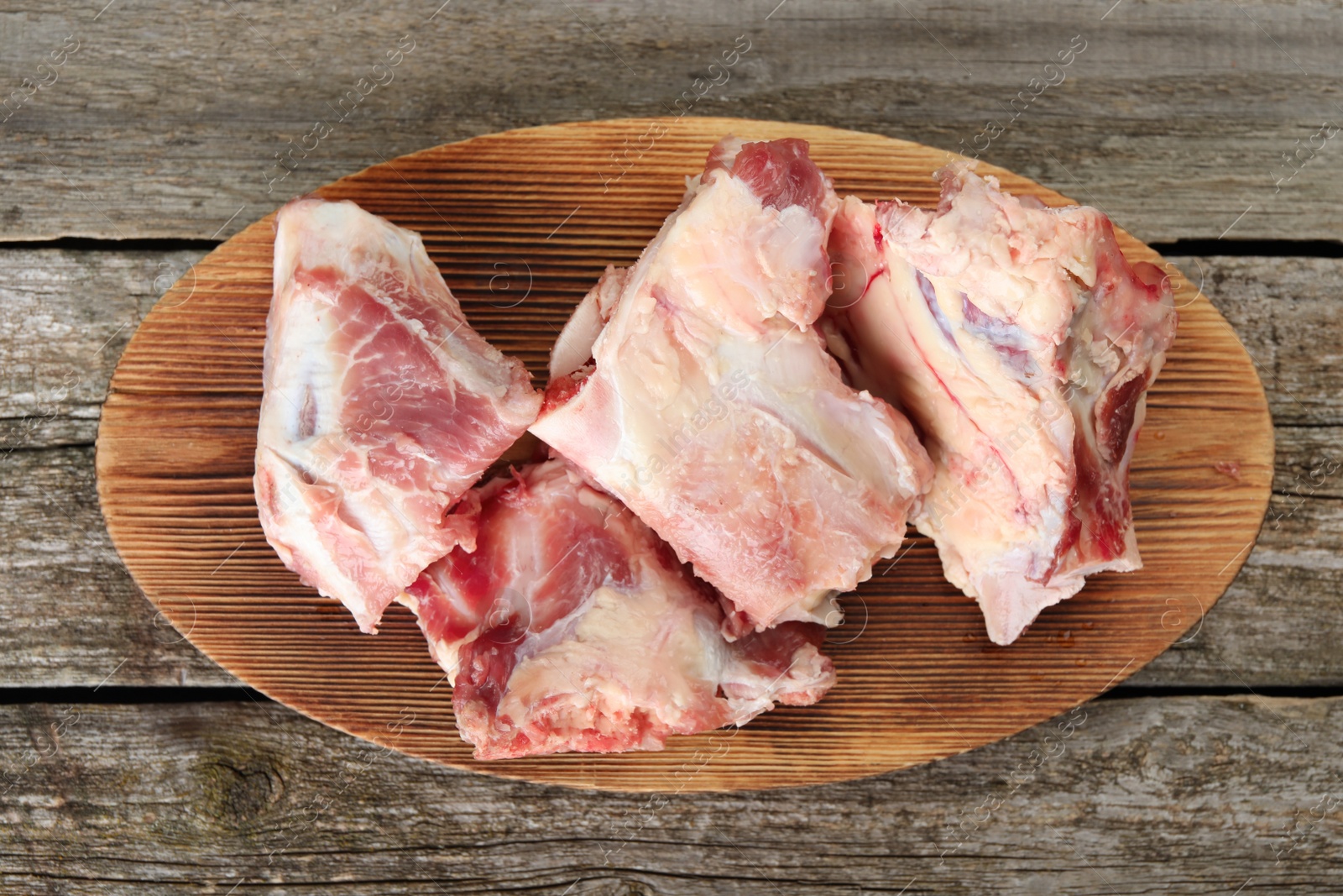 Photo of Cutting board with raw chopped meaty bones on wooden table, top view