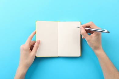 Photo of Woman writing in notebook on light blue background, top view