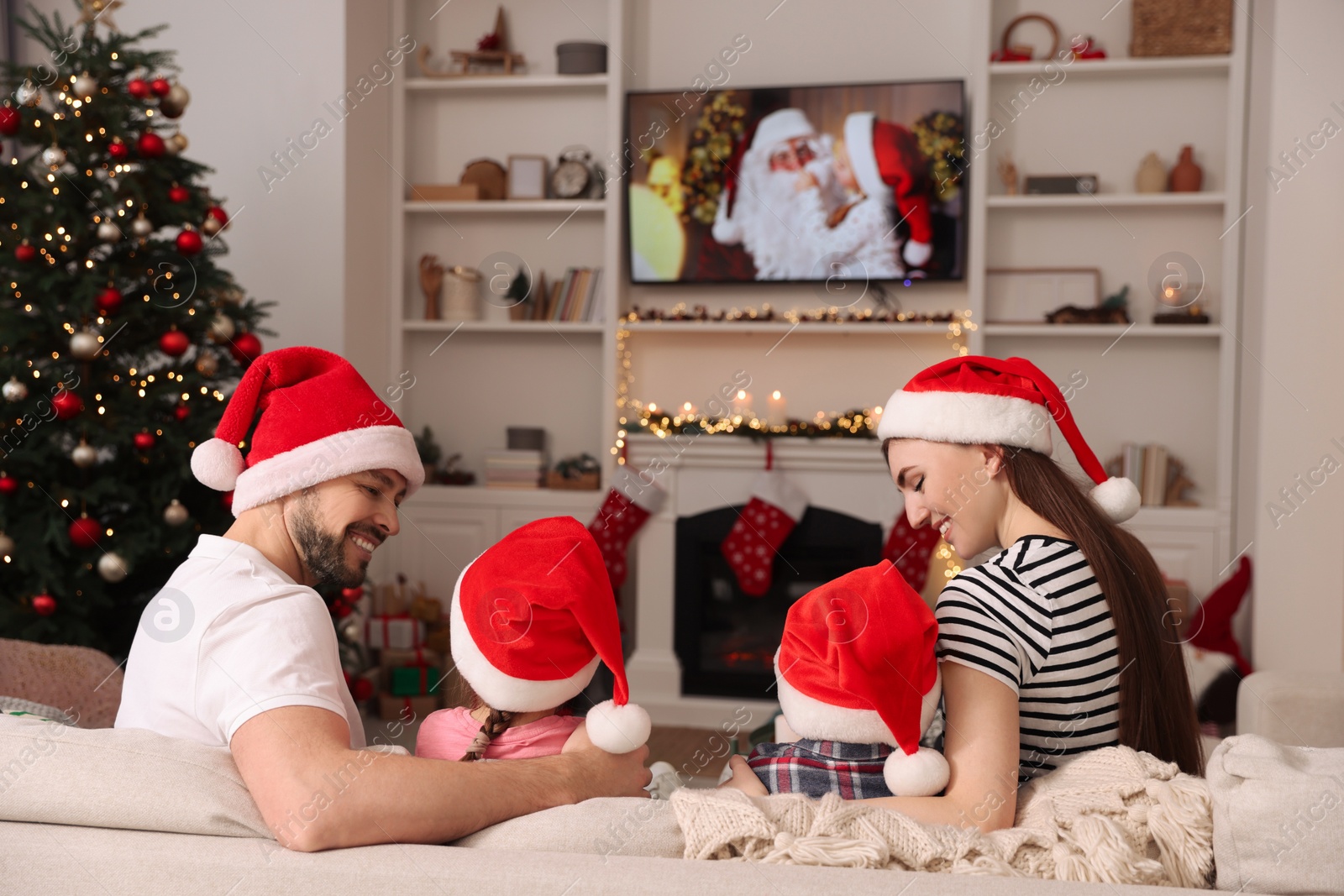 Photo of Happy family wearing Christmas hats spending time near TV in cosy room. Winter holidays atmosphere