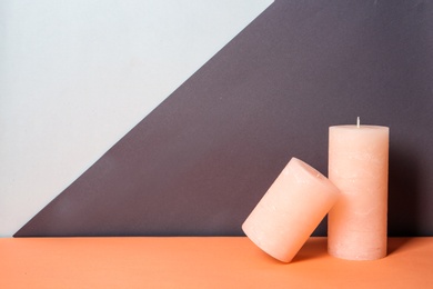 Decorative wax candles on table against color background