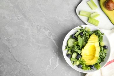 Photo of Delicious avocado salad with blueberries in bowl on grey marble table, flat lay. Space for text