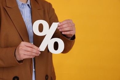 Photo of Woman holding percent sign on orange background, closeup. Space for text