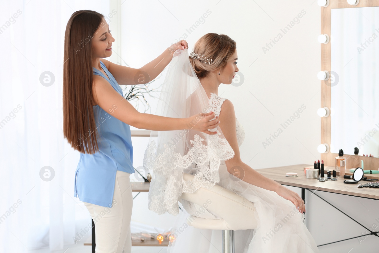 Photo of Fashion stylist preparing bride before her wedding in room