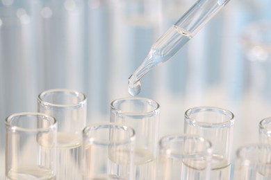 Laboratory analysis. Dripping liquid from pipette into glass test tube on blurred background, closeup