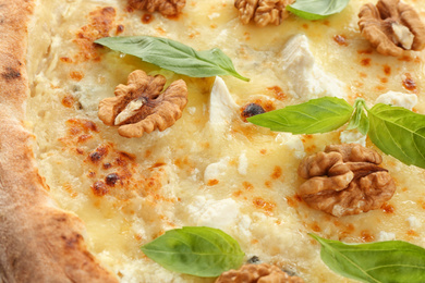 Delicious cheese pizza with walnuts and basil as background, closeup