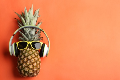 Photo of Top view of pineapple with headphones and sunglasses on orange background, space for text. Creative concept
