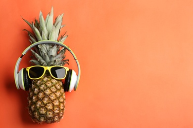 Top view of pineapple with headphones and sunglasses on orange background, space for text. Creative concept