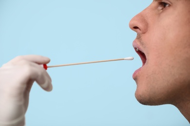 Doctor taking sample for DNA test from man on light background, closeup