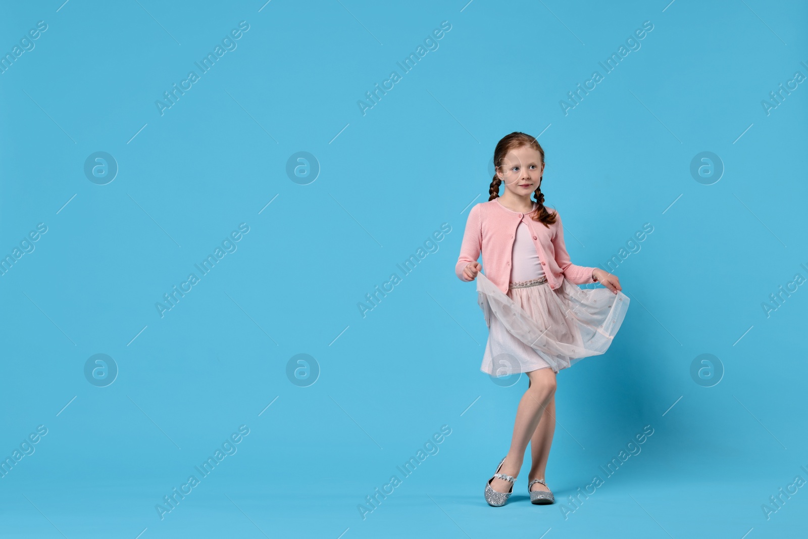 Photo of Cute little girl dancing on light blue background, space for text