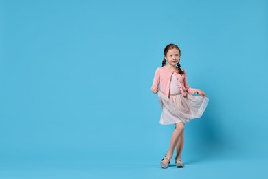 Photo of Cute little girl dancing on light blue background, space for text