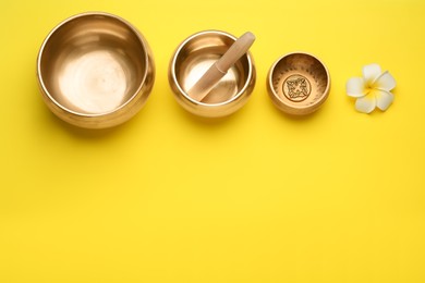 Photo of Golden singing bowls, mallet and flower on yellow background, flat lay. Space for text