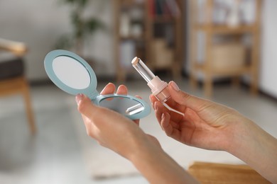 Photo of Young woman using cosmetic pocket mirror and lipstick indoors, closeup