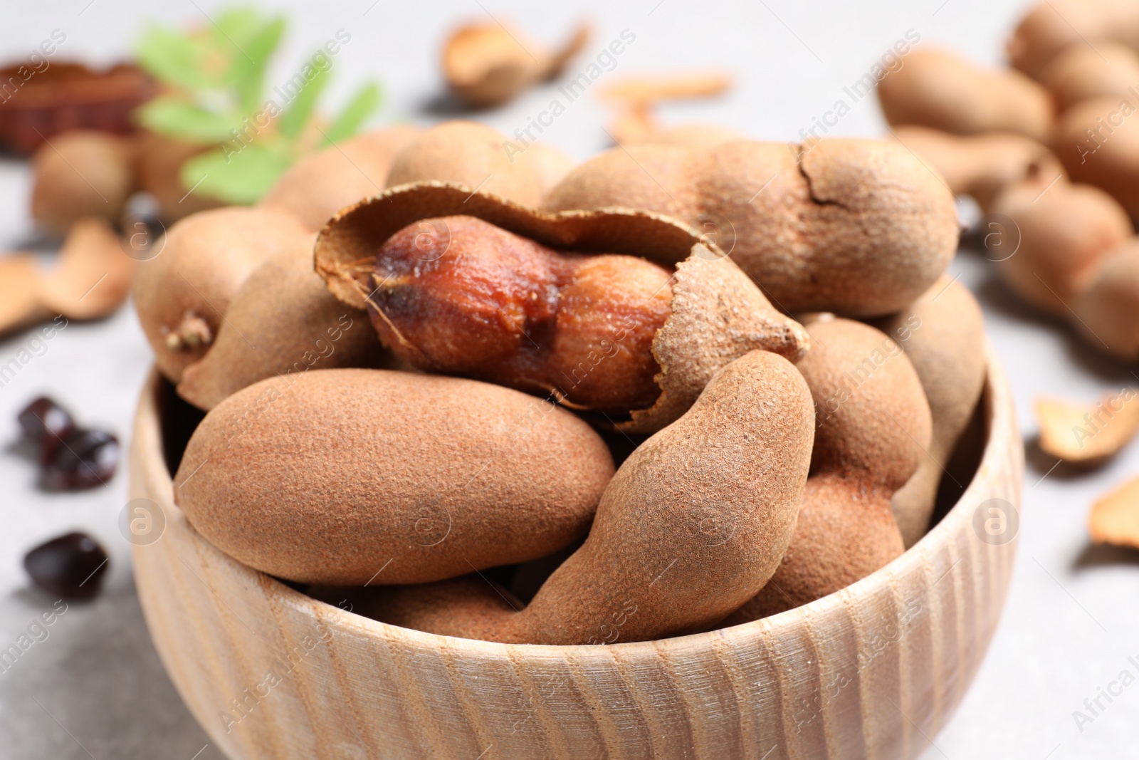 Photo of Delicious ripe tamarinds in wooden bowl on light table, closeup