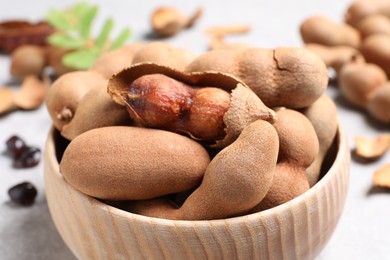 Delicious ripe tamarinds in wooden bowl on light table, closeup