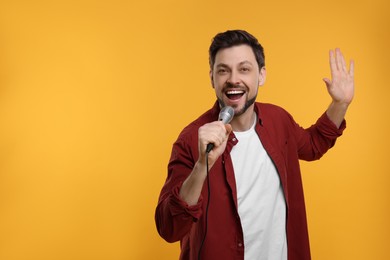 Handsome man with microphone singing on yellow background. Space for text