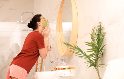 Photo of Young woman applying mask on her face near mirror in bathroom