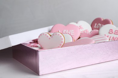 Photo of Delicious heart shaped cookies in box on white wooden table, closeup