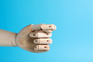 Photo of Wooden mannequin hand showing fig sign on light blue background. Space for text