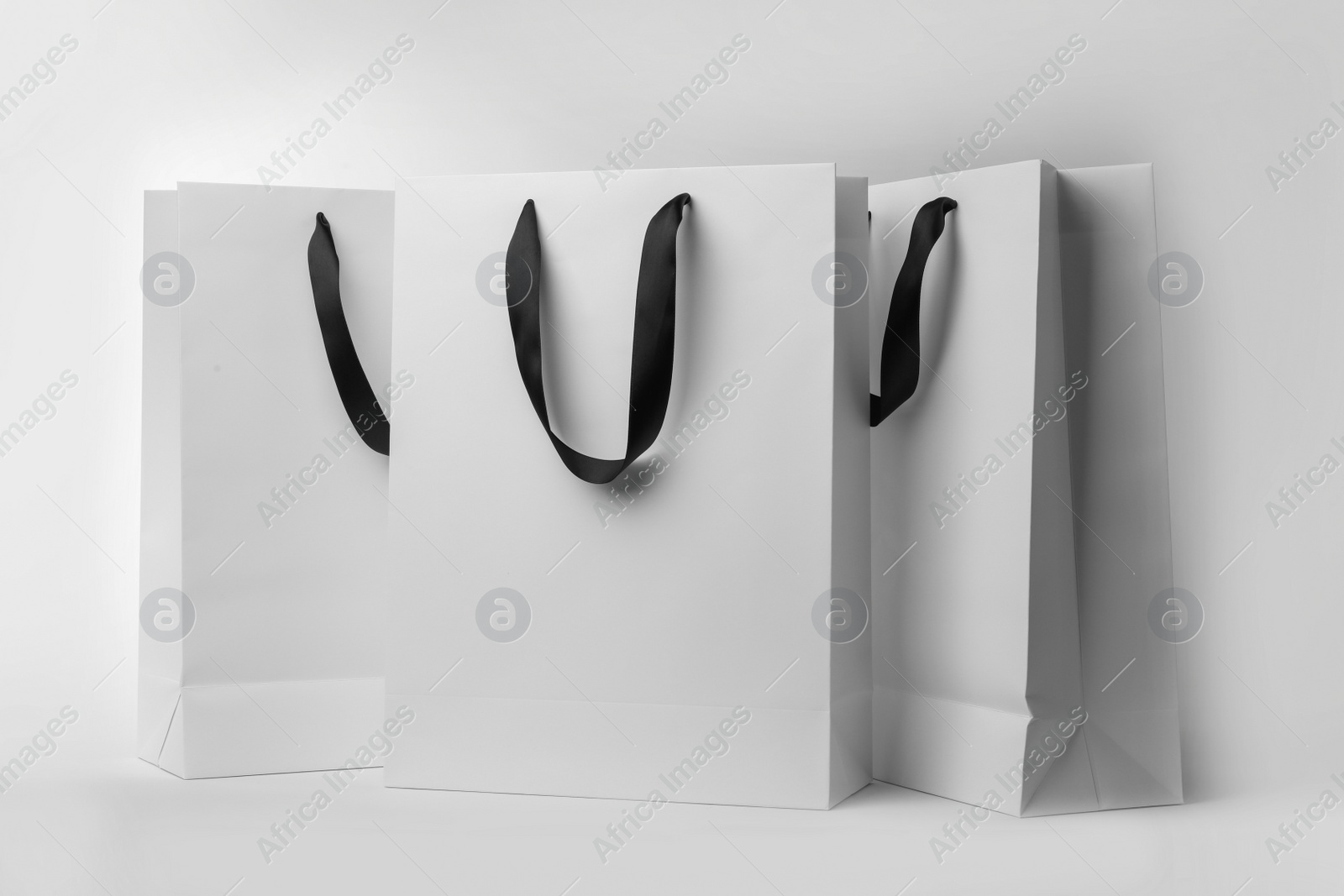 Photo of Paper shopping bags with ribbon handles on white background. Mockup for design