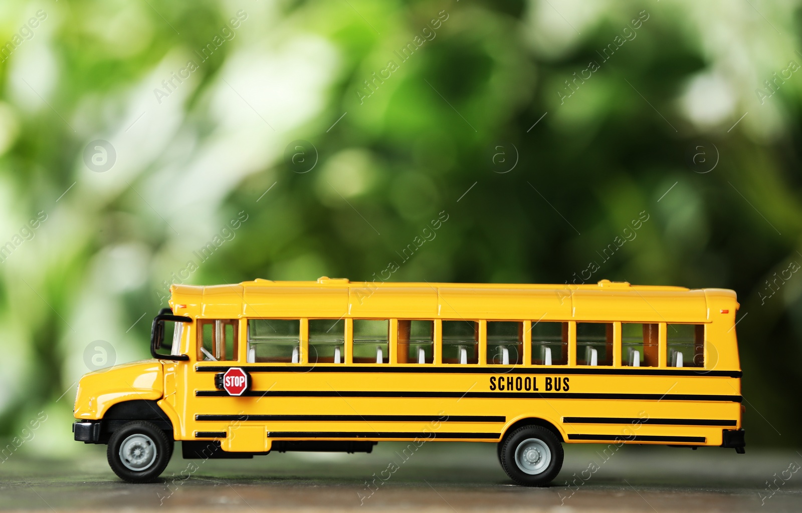 Photo of Yellow school bus on table against blurred background. Transport service