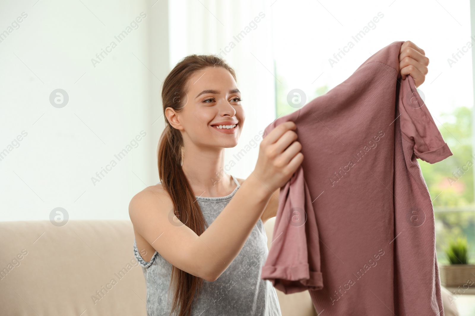Photo of Happy young woman with clean t-shirt indoors. Laundry day