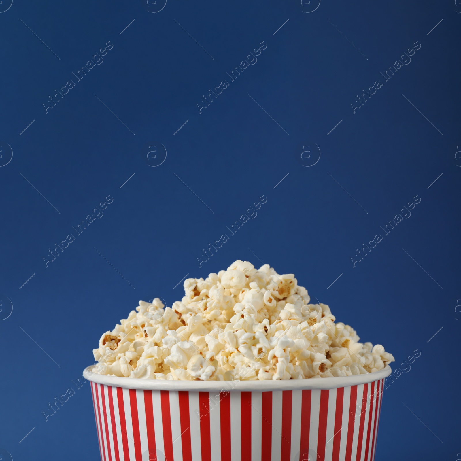 Photo of Delicious popcorn in paper bucket on blue background, closeup