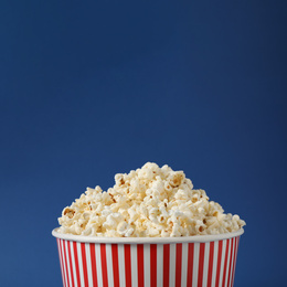 Photo of Delicious popcorn in paper bucket on blue background, closeup