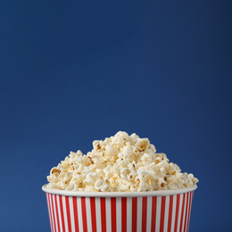 Delicious popcorn in paper bucket on blue background, closeup