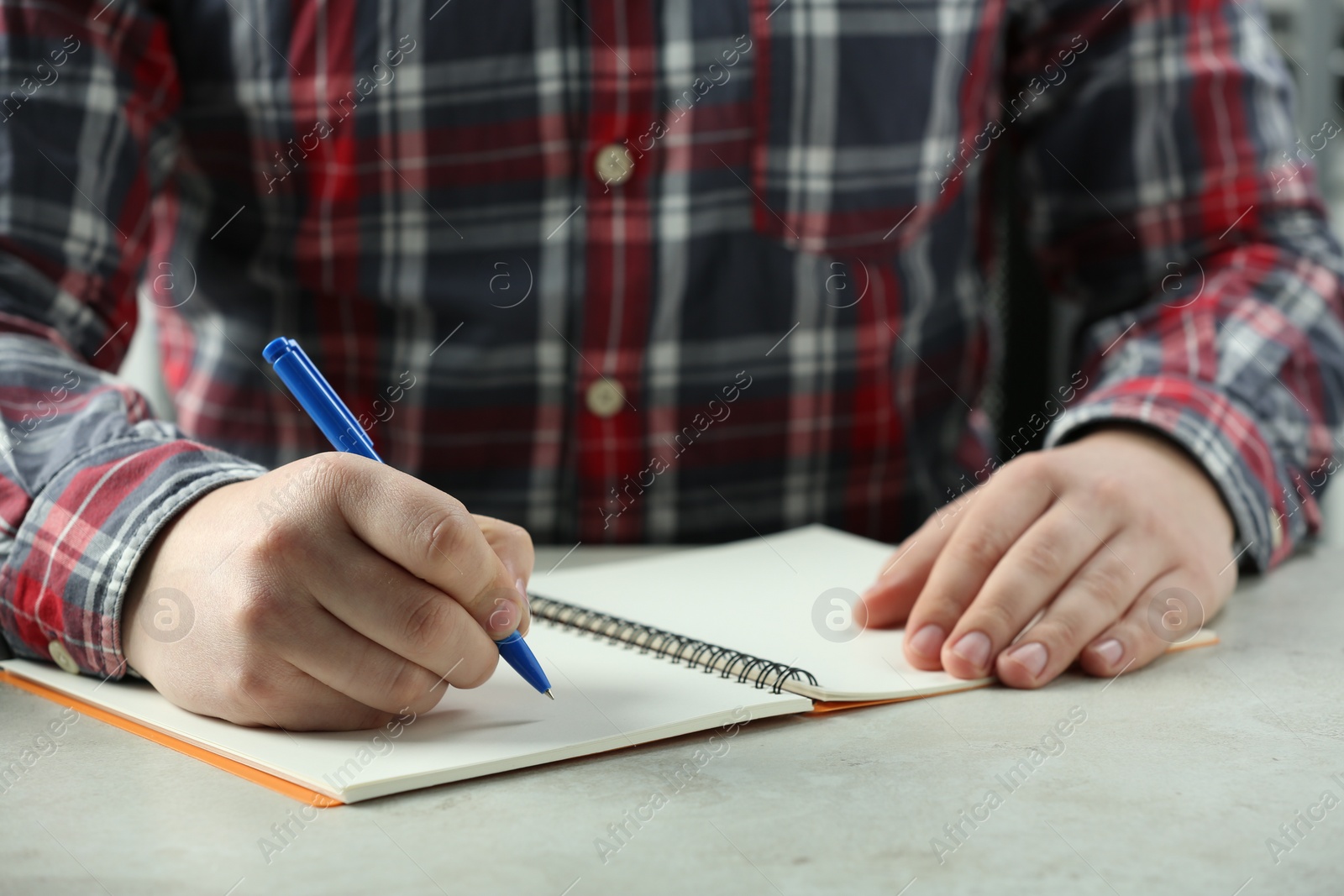 Photo of Man writing with pen in notebook at white table, closeup