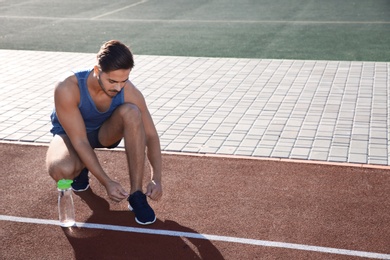 Sporty man tying shoelaces before running at stadium on sunny morning