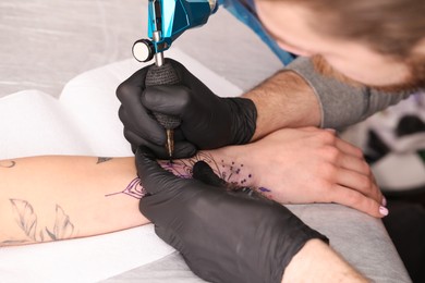 Photo of Professional artist making tattoo on hand at table, closeup