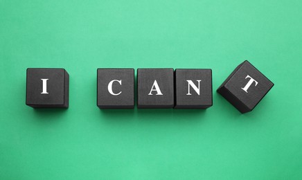 Motivation concept. Changing phrase from I Can't into I Can by removing black wooden cube with letter T on green background, flat lay
