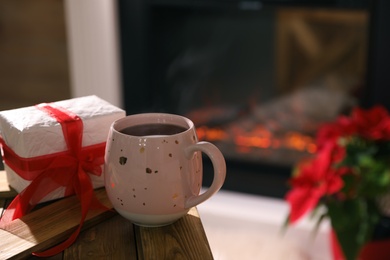 Hot drink and gift box against fireplace. Space for text