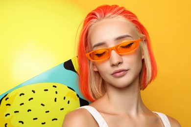 Beautiful young woman with bright dyed hair and inflatable ball on orange background