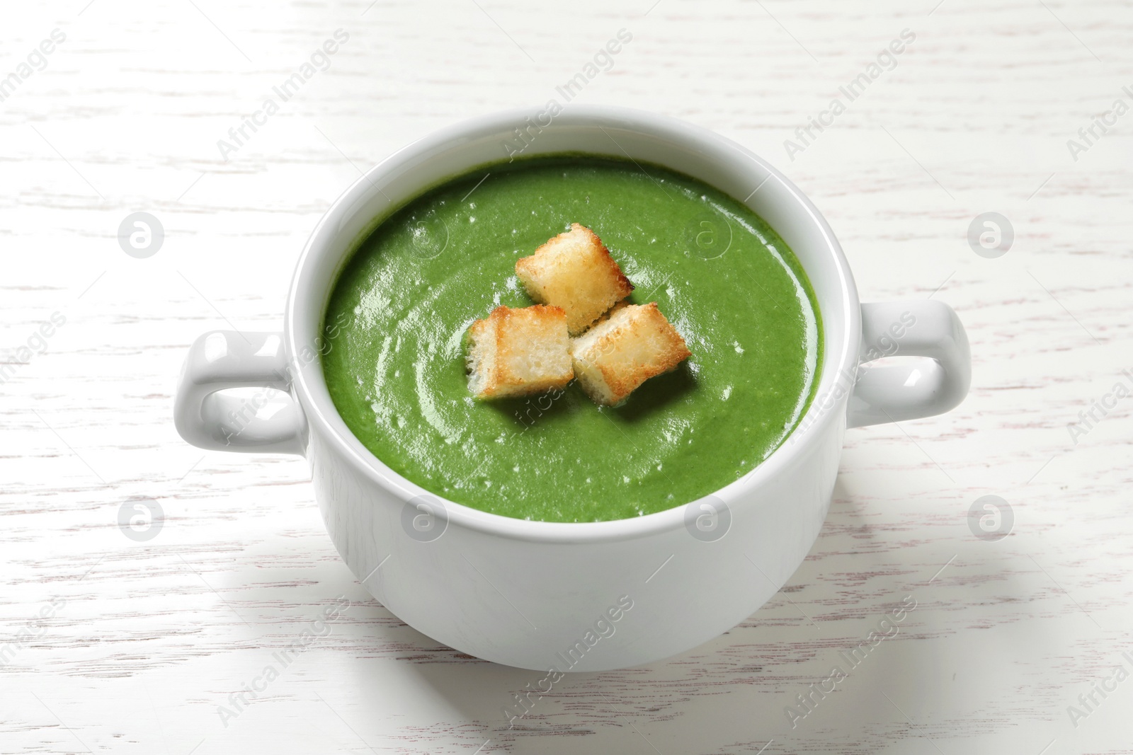 Photo of Fresh vegetable detox soup with croutons in dish on wooden table