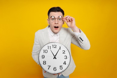 Emotional young man holding clock on orange background. Being late concept