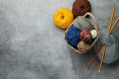 Photo of Soft woolen yarns and knitting needles on grey table, flat lay. Space for text