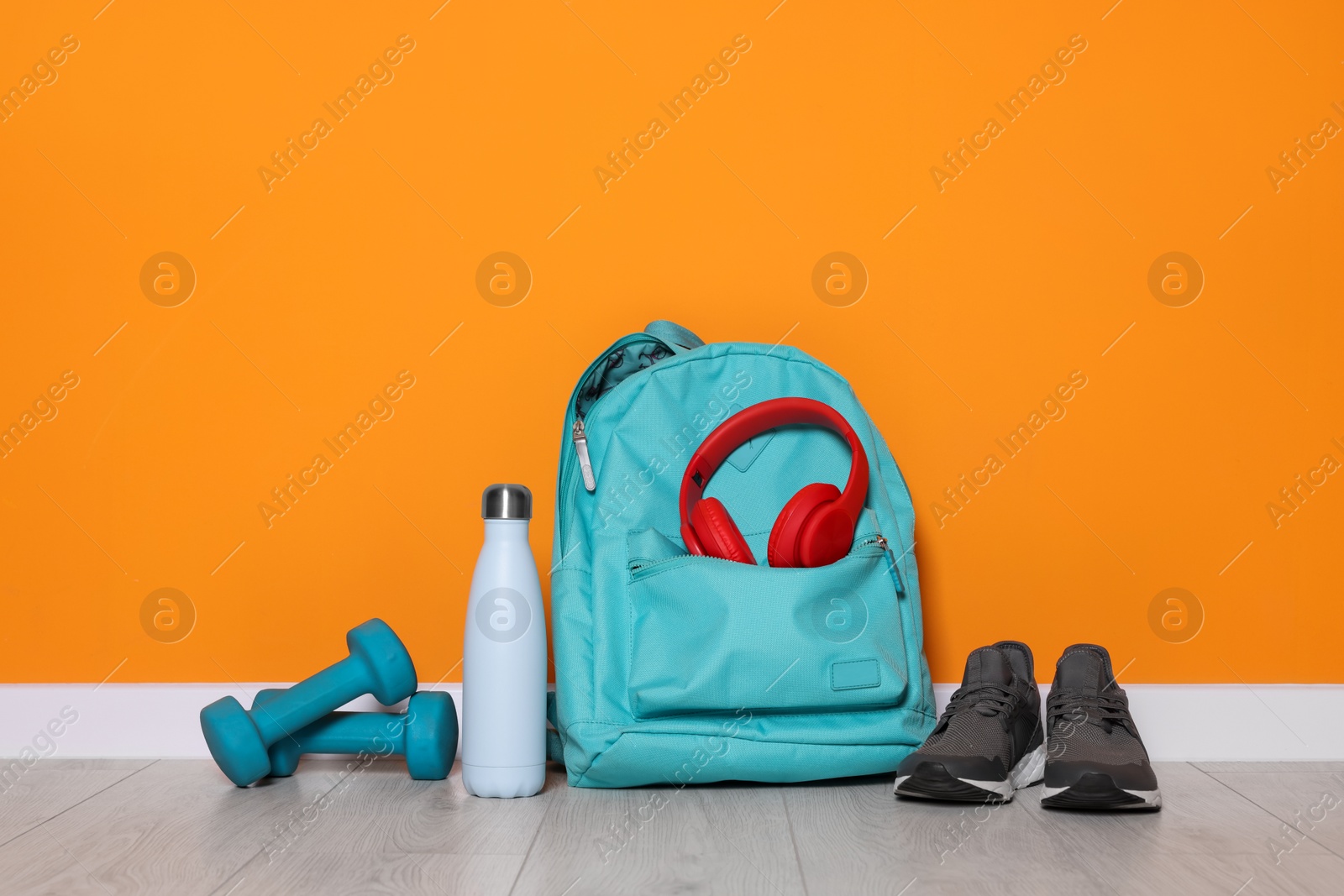 Photo of Backpack and sports equipment on floor near orange wall