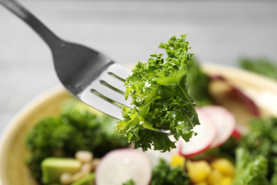 Photo of Fork with kale leaf over salad, closeup