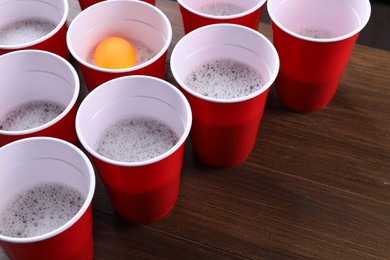 Photo of Plastic cups and ball on wooden table, space for text. Beer pong game