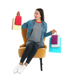 Young woman with shopping bags sitting in armchair on white background