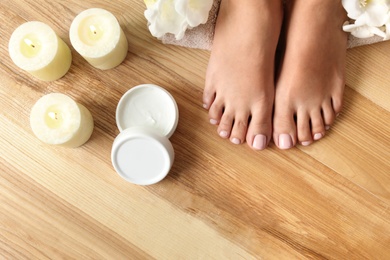 Photo of Woman with beautiful feet, candles, flowers and moisturizing cream on wooden floor, top view. Spa treatment