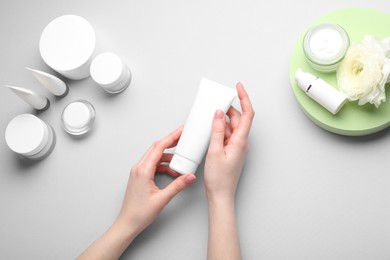 Woman holding tube of cream on light background, top view