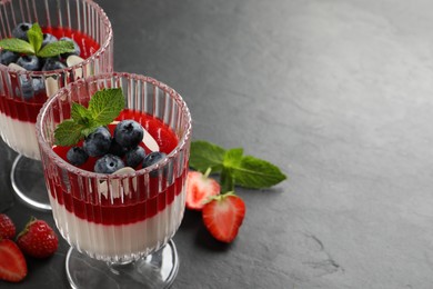 Photo of Delicious panna cotta with fruit coulis and fresh berries on dark grey table. Space for text
