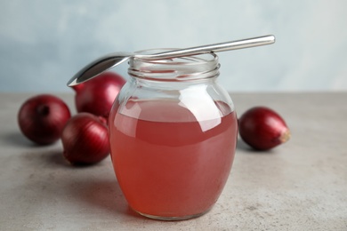 Glass jar of onion syrup with spoon and fresh vegetable on table