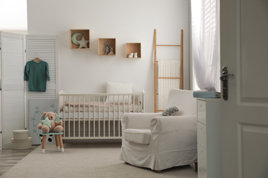 Stylish baby room interior with crib and armchair