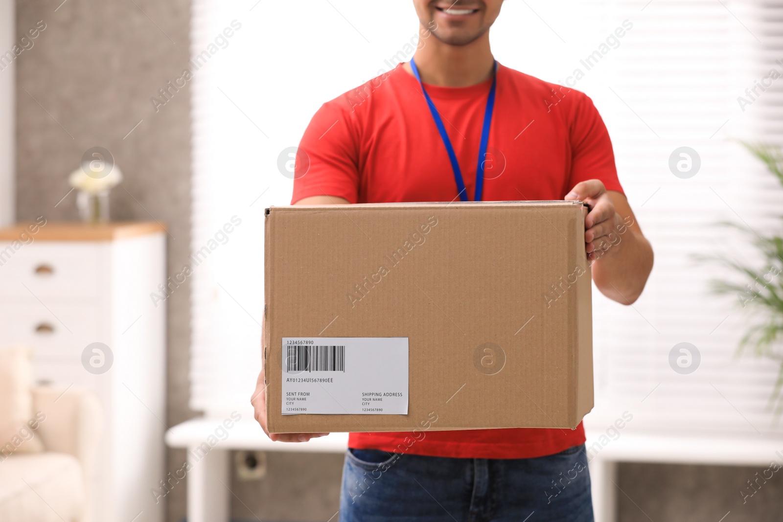 Photo of Young courier holding parcel indoors, closeup. Delivery service