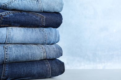 Photo of Stack of different jeans on light table against blue background. Space for text