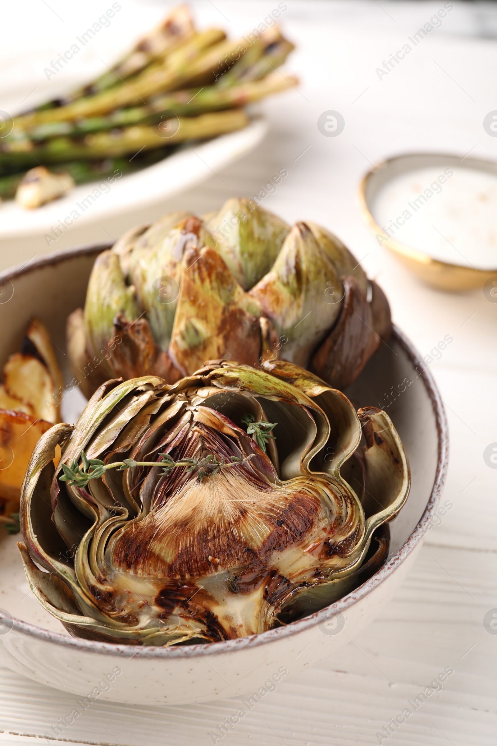 Photo of Bowl with tasty grilled artichokes on white wooden table, closeup