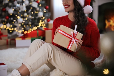 Beautiful woman with Christmas gift on floor at home, closeup